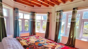 A bedroom with a wooden ceiling, a large bed with a colorful blanket, and curtains on the windows. - Kolahoi Heights  (Pahalgam)
