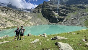 A mountainous landscape with a lake and two people standing on a grassy area. - Kolahoi Heights  (Pahalgam)