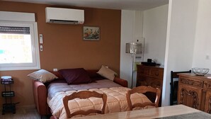 Een gezellige slaapkamer met een bed, nachtkastjes en een raam. Er is een eethoek met een tafel en stoelen.