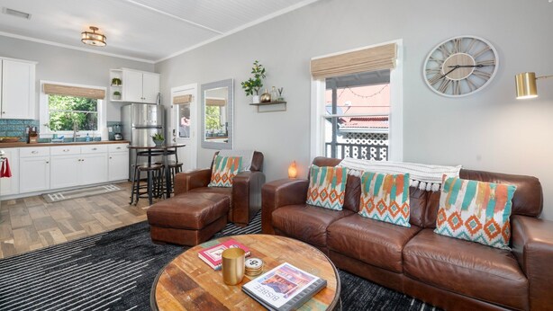 A modern living room with a brown leather sofa, a coffee table, and a kitchen in the background.