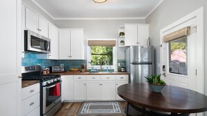 A kitchen with white cabinets, a stainless steel refrigerator, a microwave, a stove, and a dining table with a potted plant.