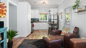 A modern kitchen with white cabinets, a stainless steel refrigerator, and a dining area with a round table and stools.