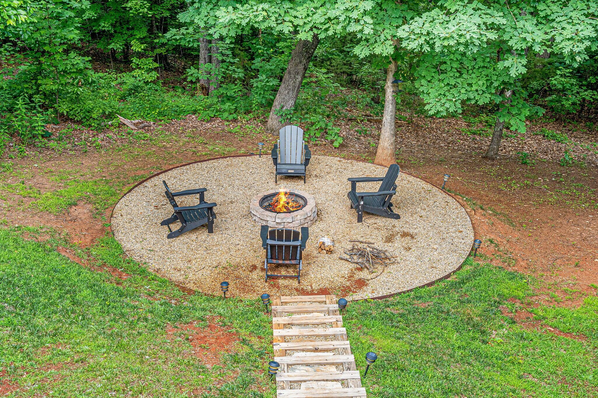 Un espacio al aire libre con una chimenea circular, cuatro sillas Adirondack y una terraza de madera que la conecta.