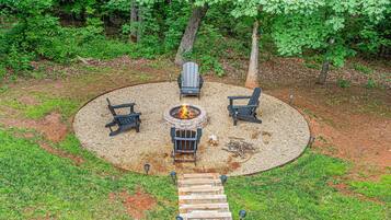 Un espacio al aire libre con una chimenea circular, cuatro sillas Adirondack y una terraza de madera que la conecta.