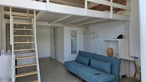 Un espacio tipo loft con un sofá azul, una escalera de madera y una pared de piedra.
