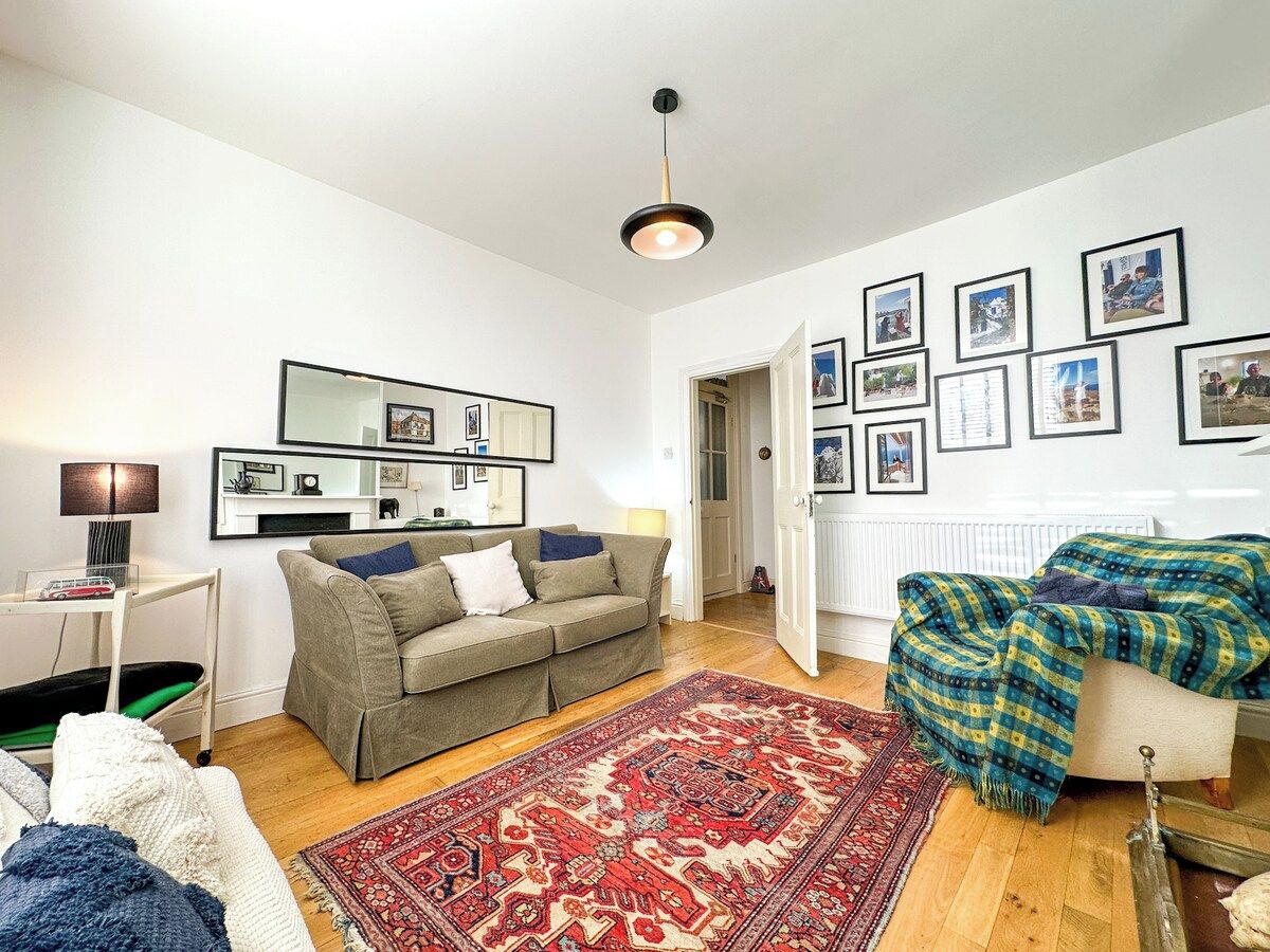 A living room with a sofa, a coffee table, a lamp, a patterned rug, and a wall with framed pictures.