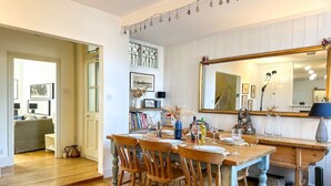 A dining area with a wooden table set for four, surrounded by chairs. A large mirror hangs above the table, reflecting the room. - NEW Cossington House - City Centre 3 Bedroom Home (Kent)