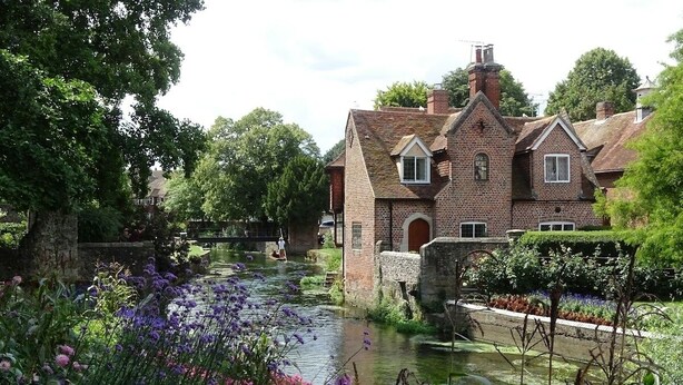 A historic brick house with a pond in the foreground, surrounded by lush greenery and flowering plants. - NEW Cossington House - City Centre 3 Bedroom Home (Kent)