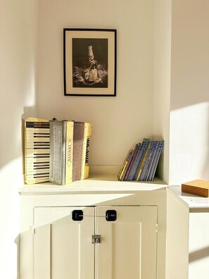 Une pièce avec un meuble blanc, un tableau encadré accroché au mur, et une pile de livres et un clavier posés sur le meuble.