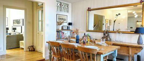 Comedor con mesa de madera dispuesta para cuatro personas, rodeada de sillas y un espejo grande sobre la mesa.