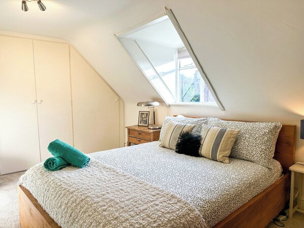 Une chambre avec un plafond en pente, un lit avec une literie à motifs, une table de chevet avec une lampe et une fenêtre donnant sur un beau paysage.