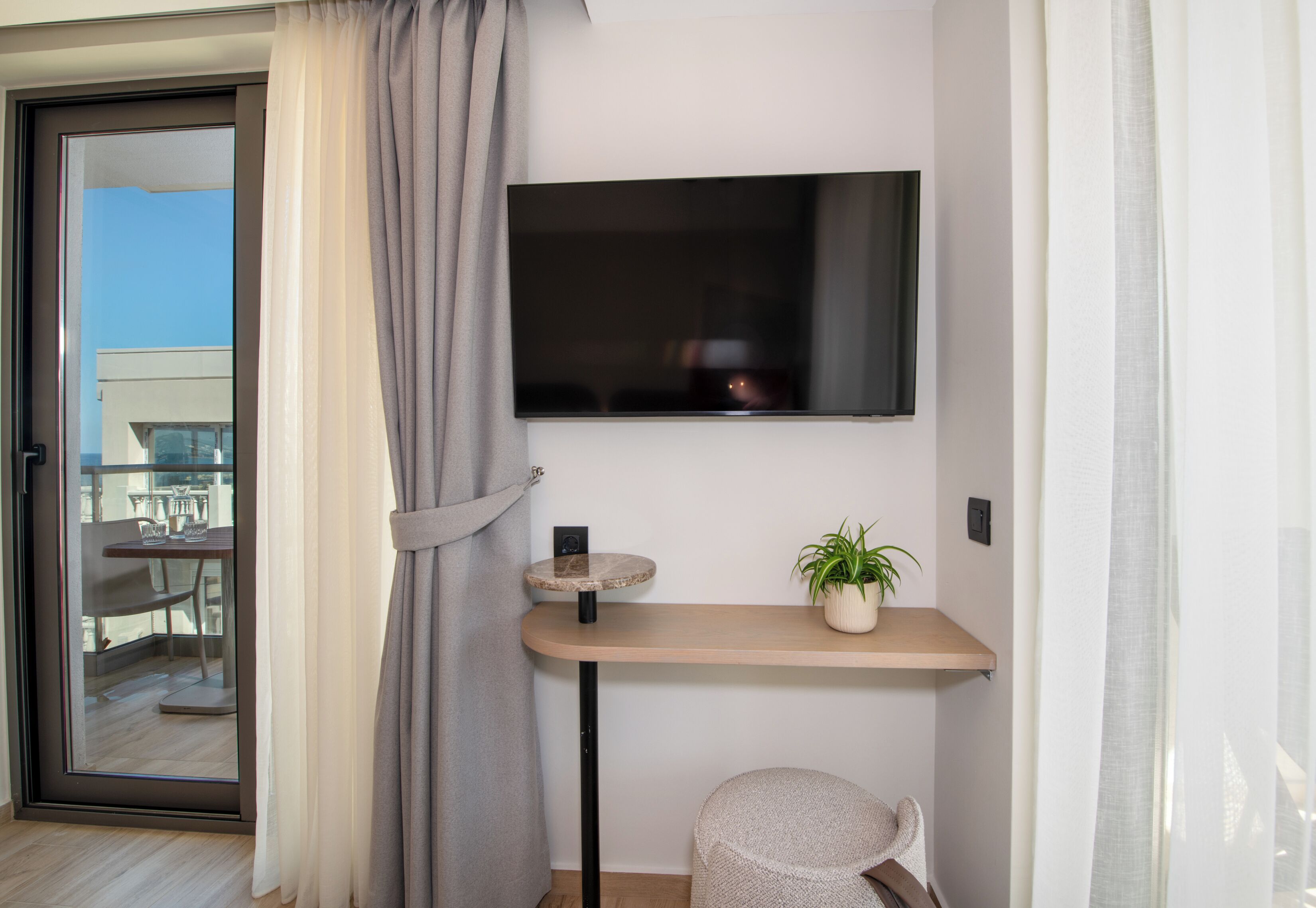 A modern living room with a flat-screen TV mounted on the wall, a small round table with a potted plant, and a cozy seating area with a chair.
