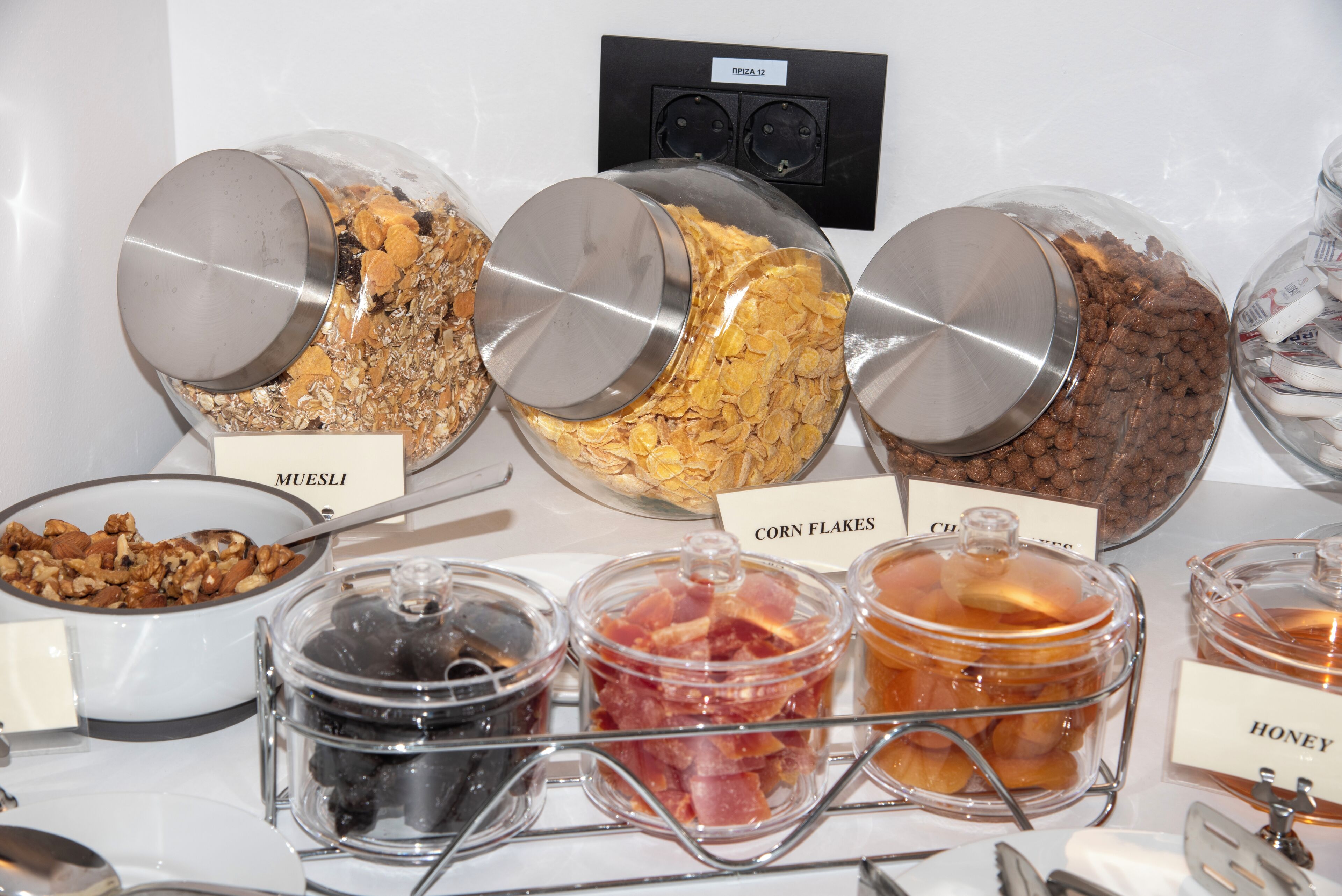 Einbufett mit beschrifteten Speisebehältern, darunter Müsli, Cornflakes und Honig.