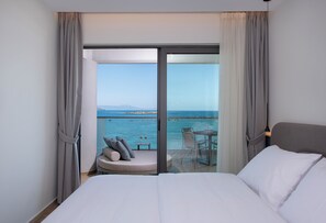 A hotel room with a large bed, a small seating area with a table, and a balcony with a view of the sea. -  EdgeWater Beach Hotel (Chania)