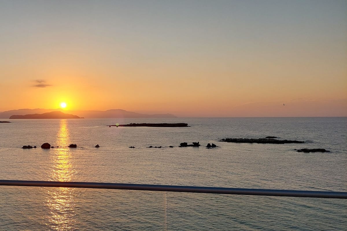 A sunset over a calm sea with distant landforms and a clear sky.