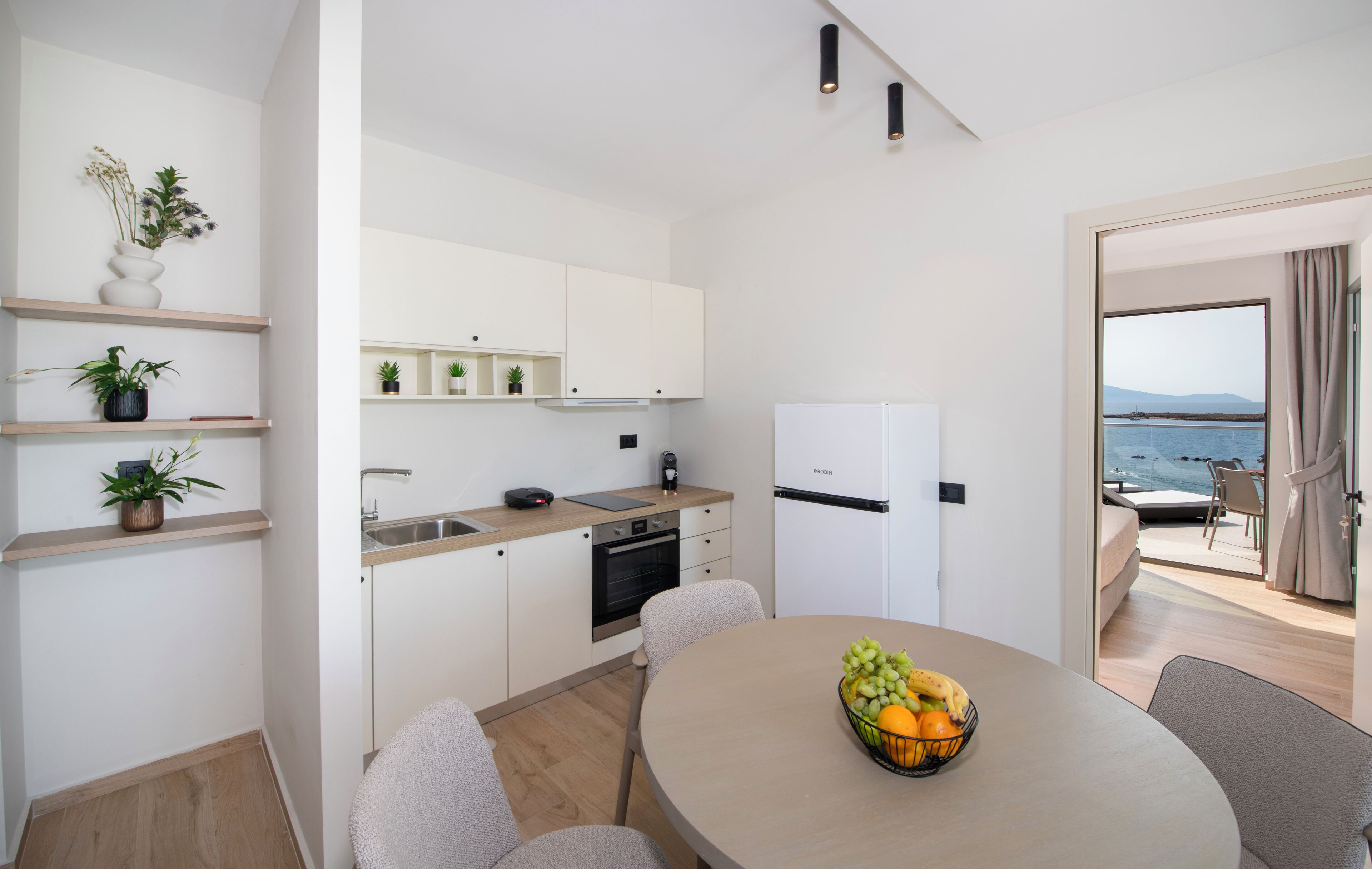 Una cocina moderna con armarios blancos, una zona de comedor con mesa redonda y vistas al mar a través de un ventanal.