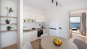 Una cocina moderna con armarios blancos, una zona de comedor con mesa redonda y vistas al mar a través de un ventanal.