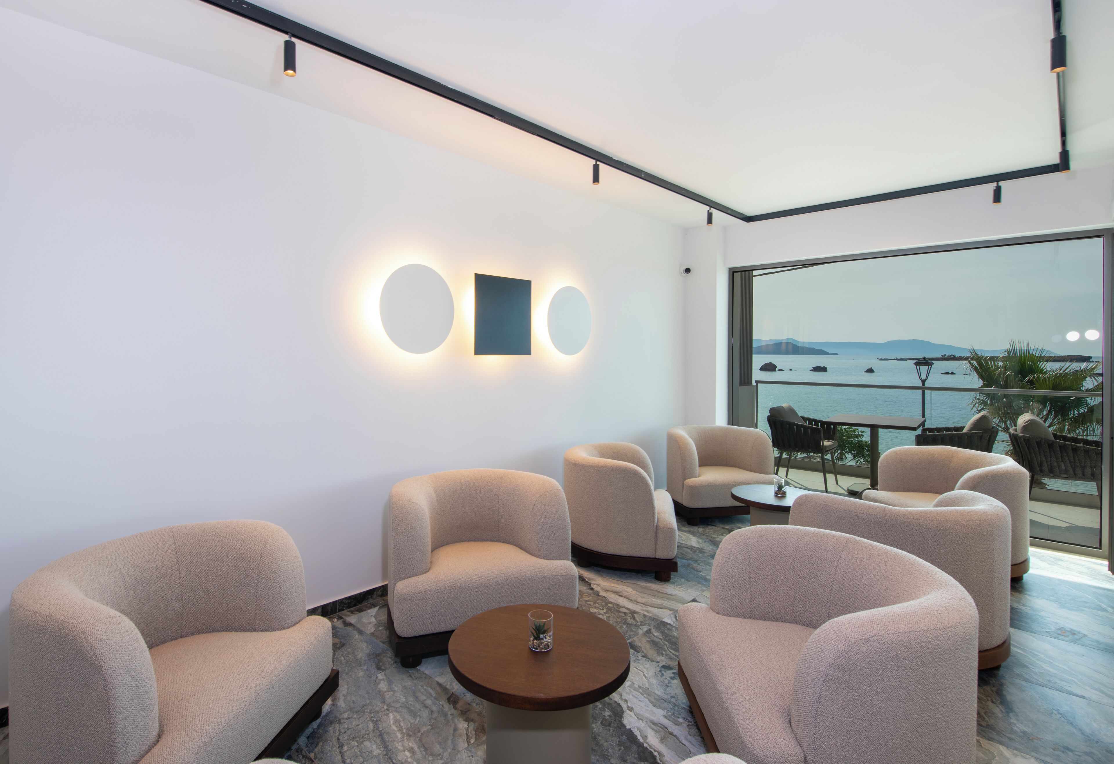 A modern lounge with plush seating, a marble floor, and a large window offering a view of the sea.