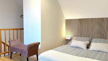 A bedroom with a bed, a chair, a wooden headboard, and a wall-mounted light fixture.