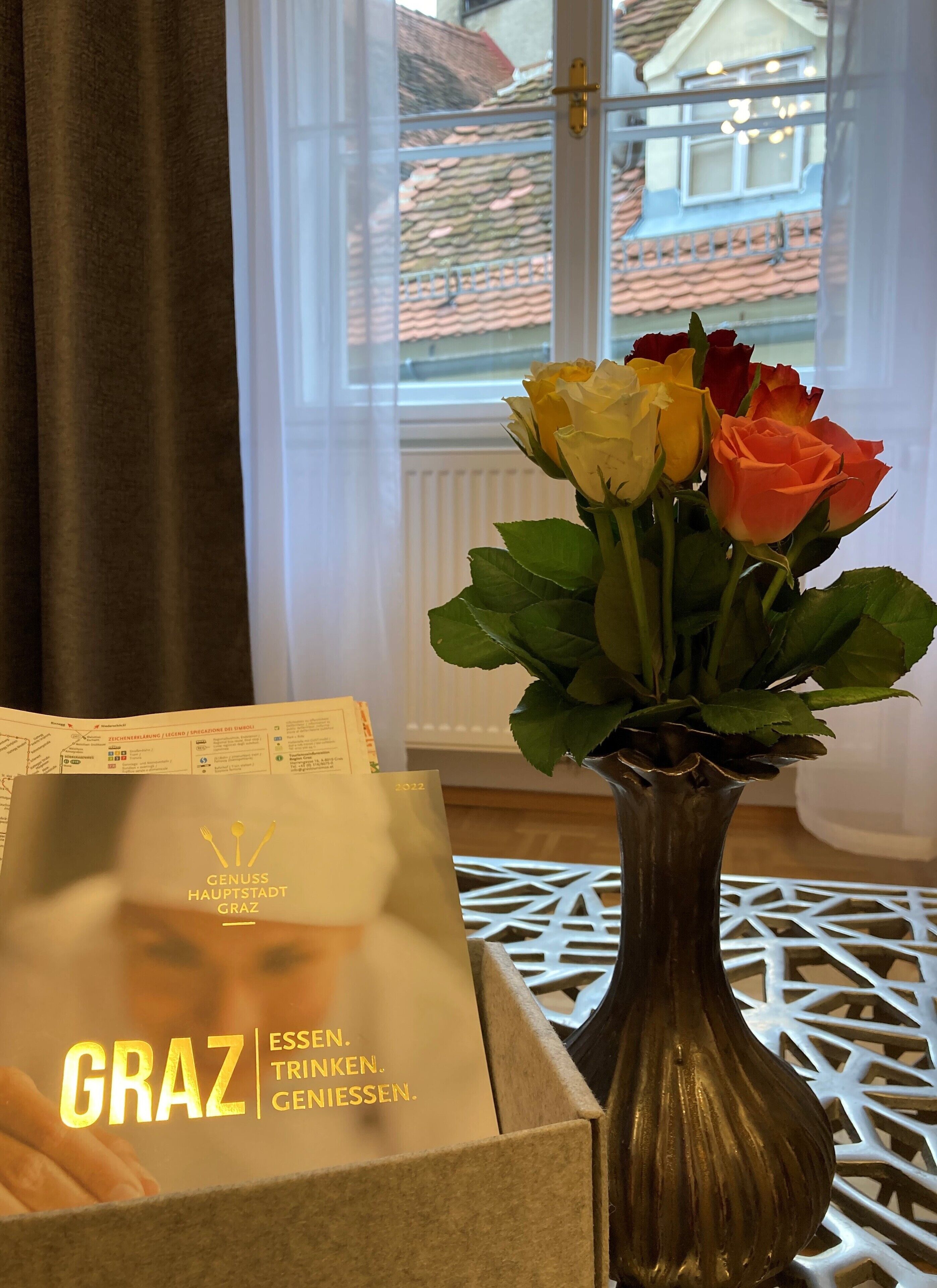 Eine Vase mit Rosen und eine Schachtel mit Text auf einem Tisch in der Nähe eines Fensters.