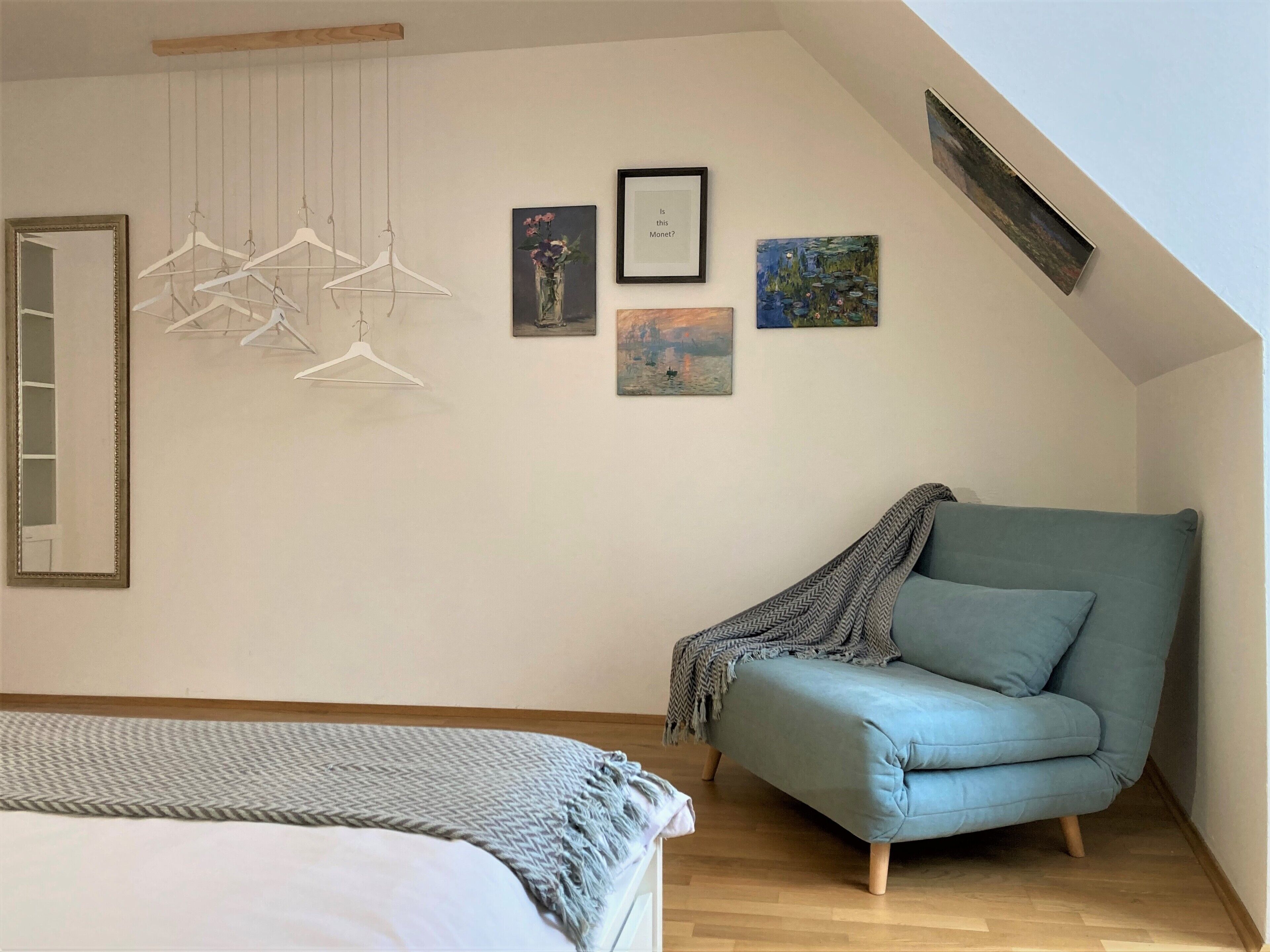 Ein Schlafzimmer mit einem Bett, einem blauen Sessel und Wandbildern, darunter ein Gemälde von Monet.