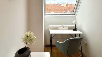A modern room with a sloped ceiling, a skylight, a white desk, a grey chair, a white radiator, and a wall clock.