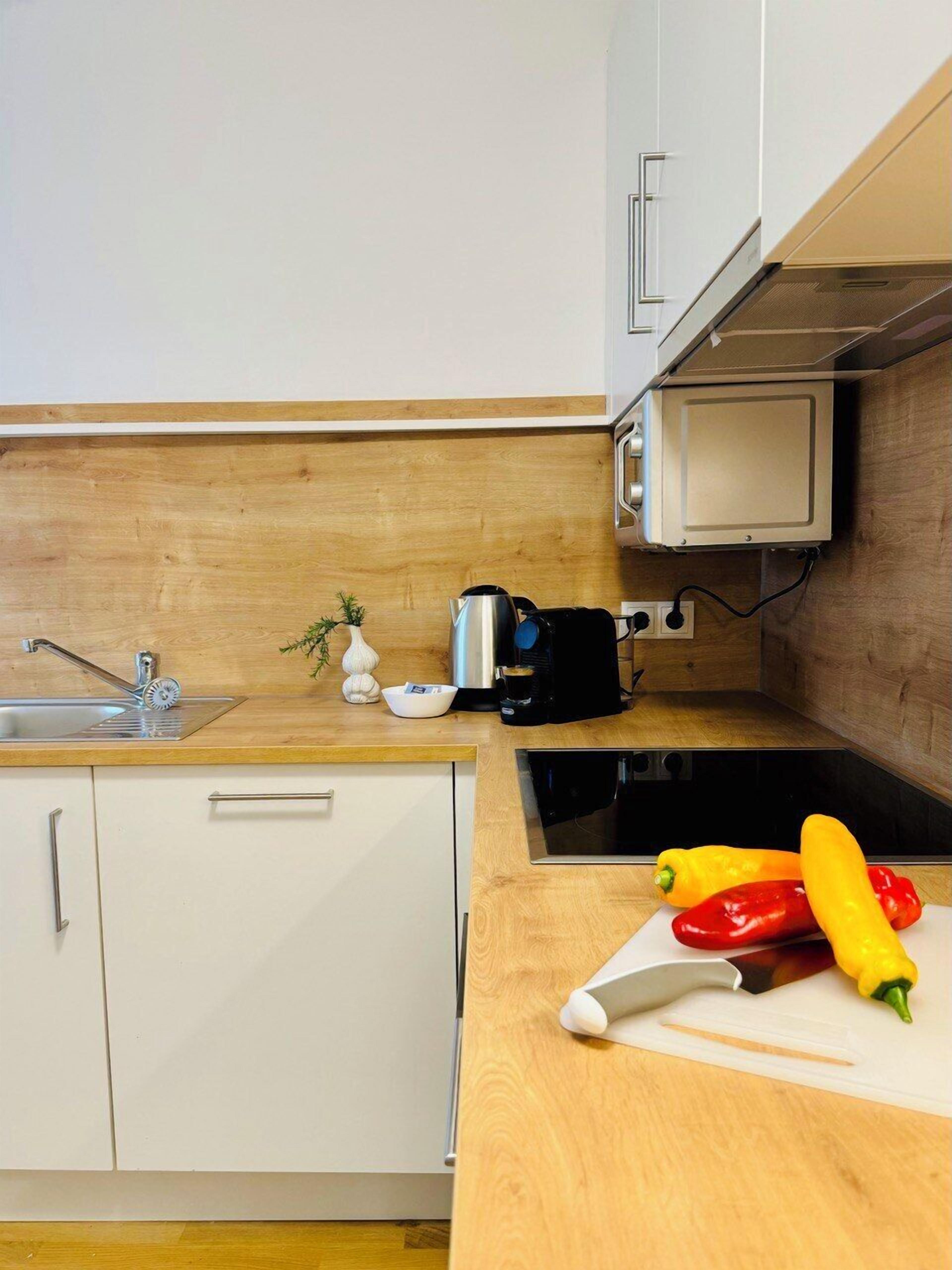 Eine Küche mit Holzausziehtisch, Spüle, Schränken, einer Kaffeemaschine und einem Schneidebrett mit Gemüse.