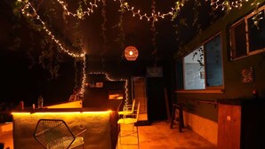 A dimly lit bar area with a counter, chairs, and string lights. - Varuna Home (Tulum)
