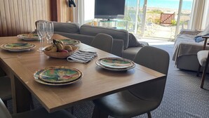 Comedor con una mesa lista para cuatro personas, un televisor y vista a la playa.