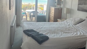 Un dormitorio con cama, vista a la playa y balcón con mobiliario exterior.