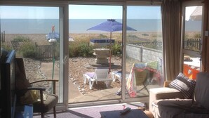 Una sala de estar con vista a la playa, un patio con mobiliario exterior y un puerta corrediza que da al patio.