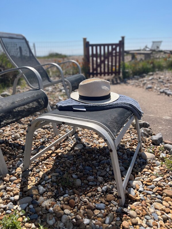 A beach chair with a straw hat on it, placed on pebbles.