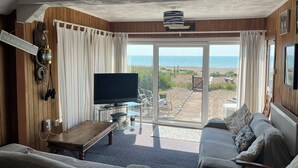 Una sala de estar acogedora con un televisor grande, paredes de madera, un sofá y vista al mar a través de un ventanal.