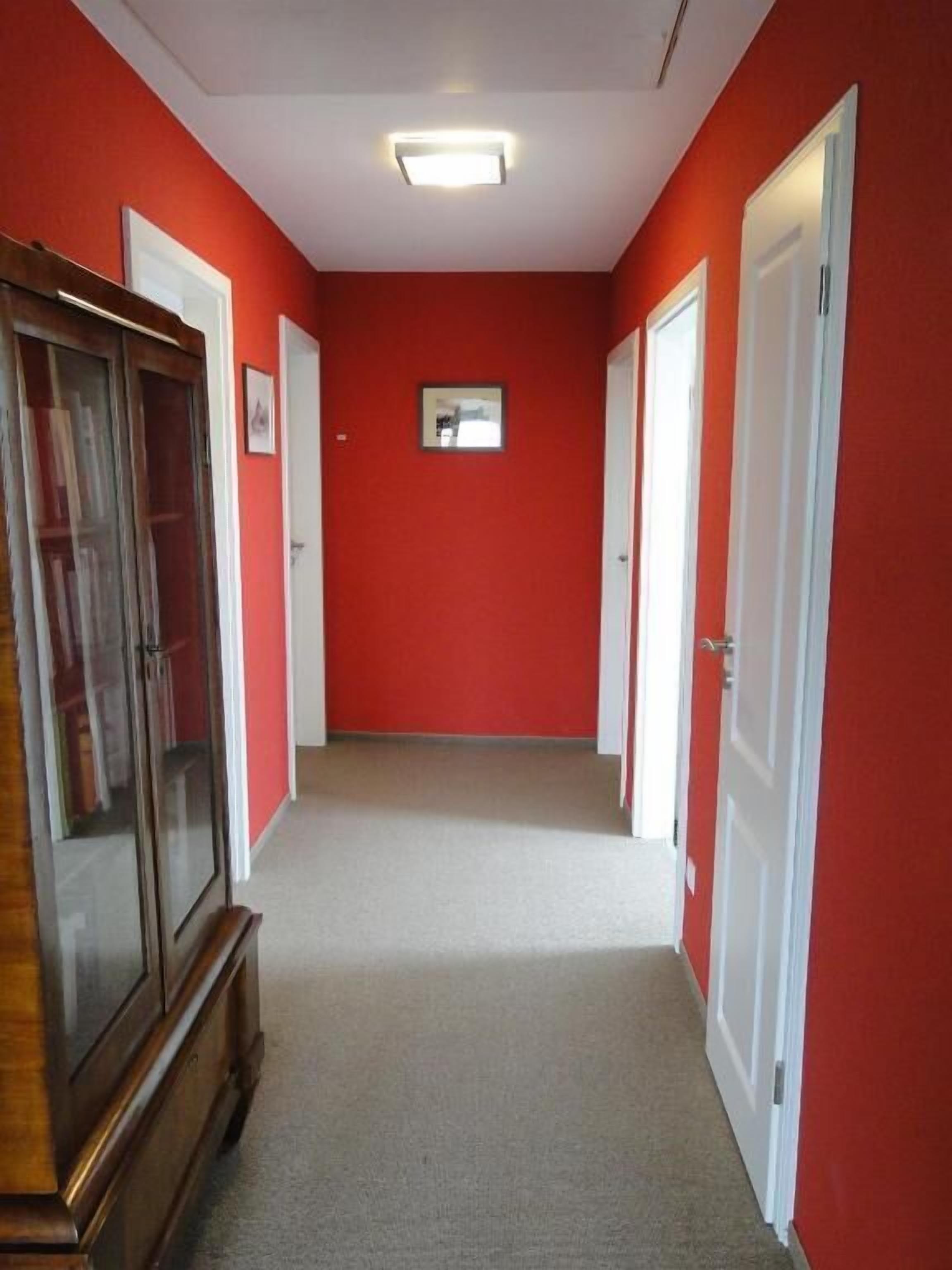 A hallway with red walls, white doors, and a carpeted floor.