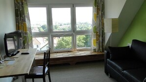 A room with a desk, a chair, a black sofa, and a large window with curtains. - Pension Villa am Burgberg (Waltershausen)