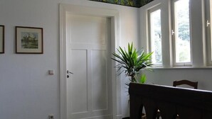 A room with a white door, a dining table with chairs, a potted plant, and a window with a view of greenery. - Pension Villa am Burgberg (Waltershausen)