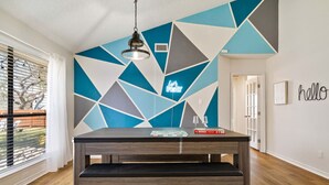 Un salon moderne avec un mur orné d’un motif géométrique, une table basse en bois foncé et un luminaire suspendu.