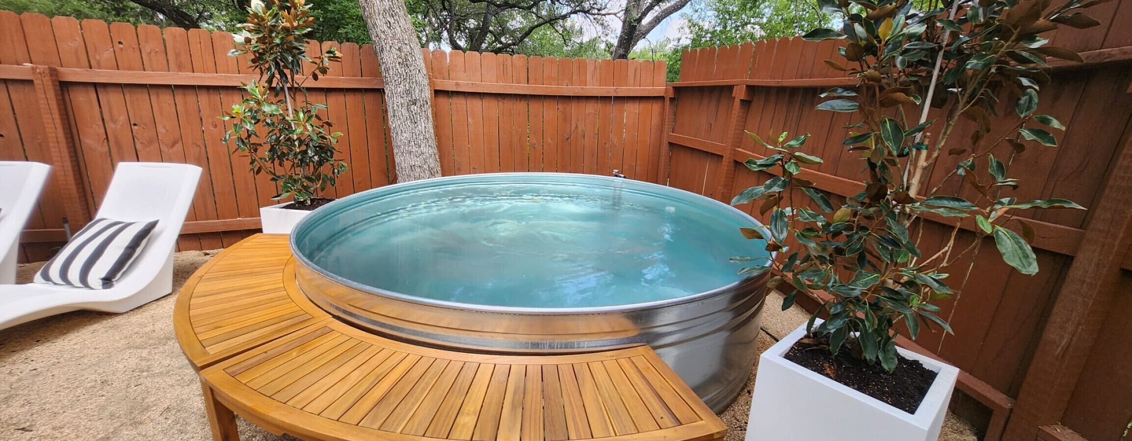 A hot tub with a wooden deck, surrounded by a wooden fence and potted plants.