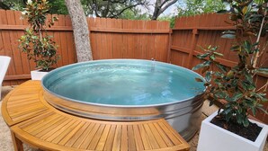 Un bain à remous avec une terrasse en bois, entouré d’une clôture en bois et agrémenté de plantes en pot.