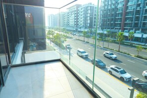 A modern building with large windows overlooking a busy street with cars and palm trees. - Bloomfields Lovely 1BHK Azizi Riviera (Dubai)