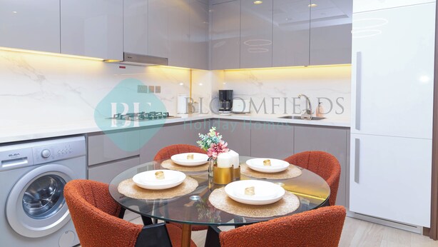 A modern kitchen with a glass dining table, orange chairs, and a washing machine.