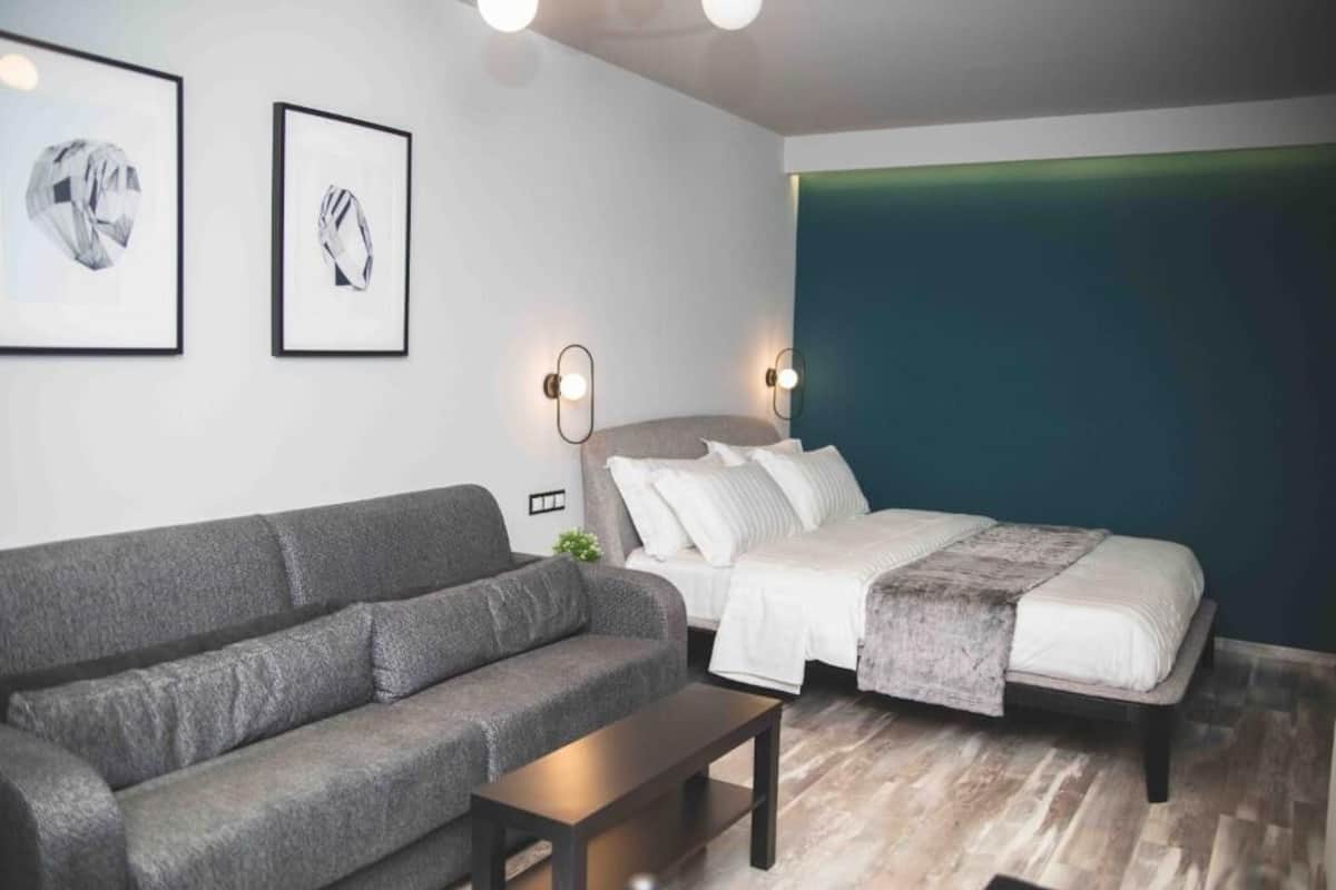 A modern bedroom with a grey sofa, a bed with white bedding, and two framed pictures on the wall.