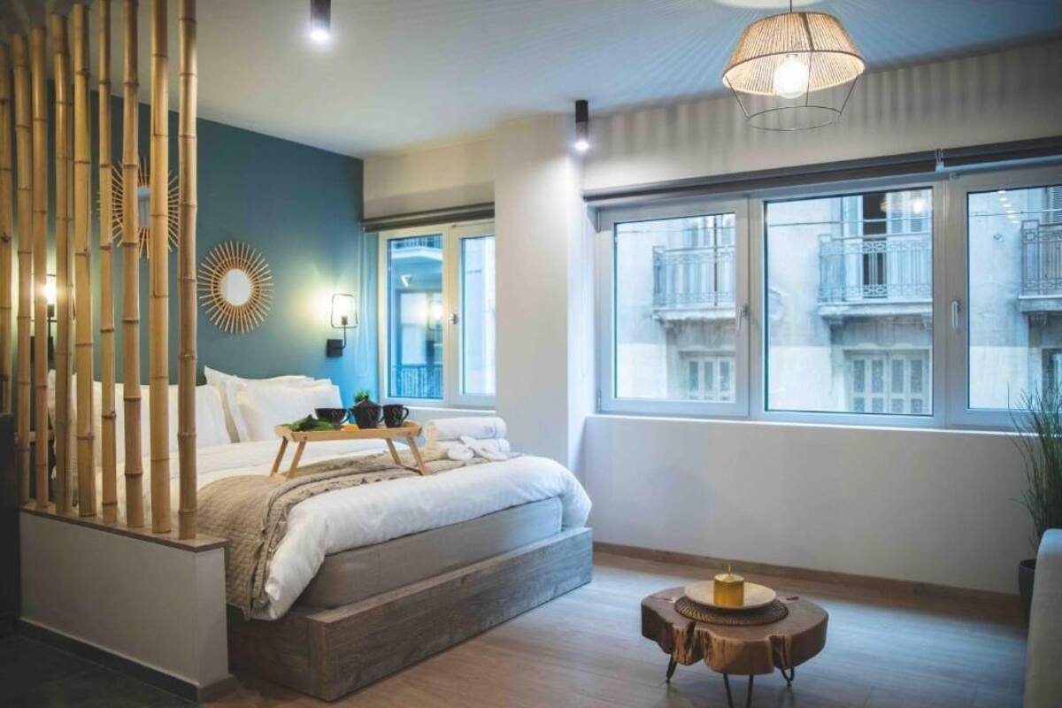 A modern bedroom with a bed, bedside table, and a large window with a view of buildings.