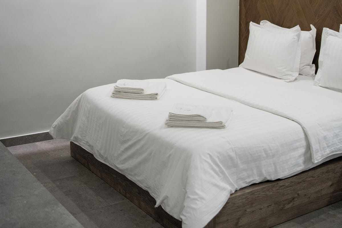 A modern bedroom with a wooden headboard, a neatly made bed with white linens, and a large window providing natural light.