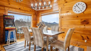 A wooden cabin interior with a dining table, chairs, a clock, a chandelier, and a video game console. - Moonlight Ridge! Mtn views! Hot tub! Pool! (Sevierville)