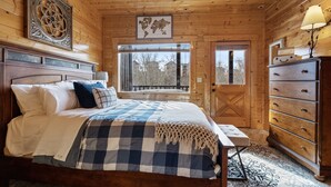 A wooden cabin bedroom with a large bed, a dresser, a window with a view, and a world map on the wall. - Moonlight Ridge! Mtn views! Hot tub! Pool! (Sevierville)