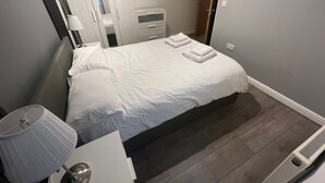 A neatly made bed with white linens, a bedside table with a lamp, and a wardrobe with a mirror.
