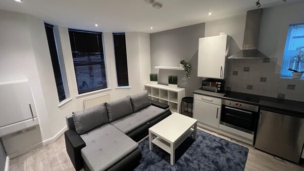 A modern kitchen with built-in appliances, a grey sofa, and a small dining table.