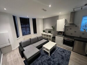 Eine moderne Küche mit integrierten Geräten, ein graues Sofa und ein kleiner Esstisch.