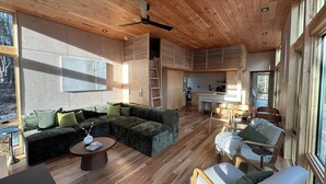 A spacious living area with a wooden ceiling, a large L-shaped sofa, a coffee table, and a dining area with chairs and a small table.